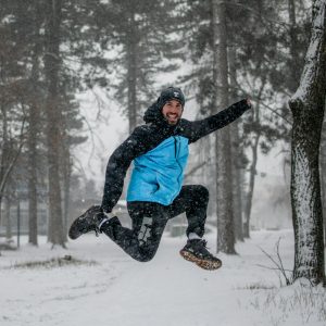 man in blue jacket and black pants sitting on snow covered ground during daytime